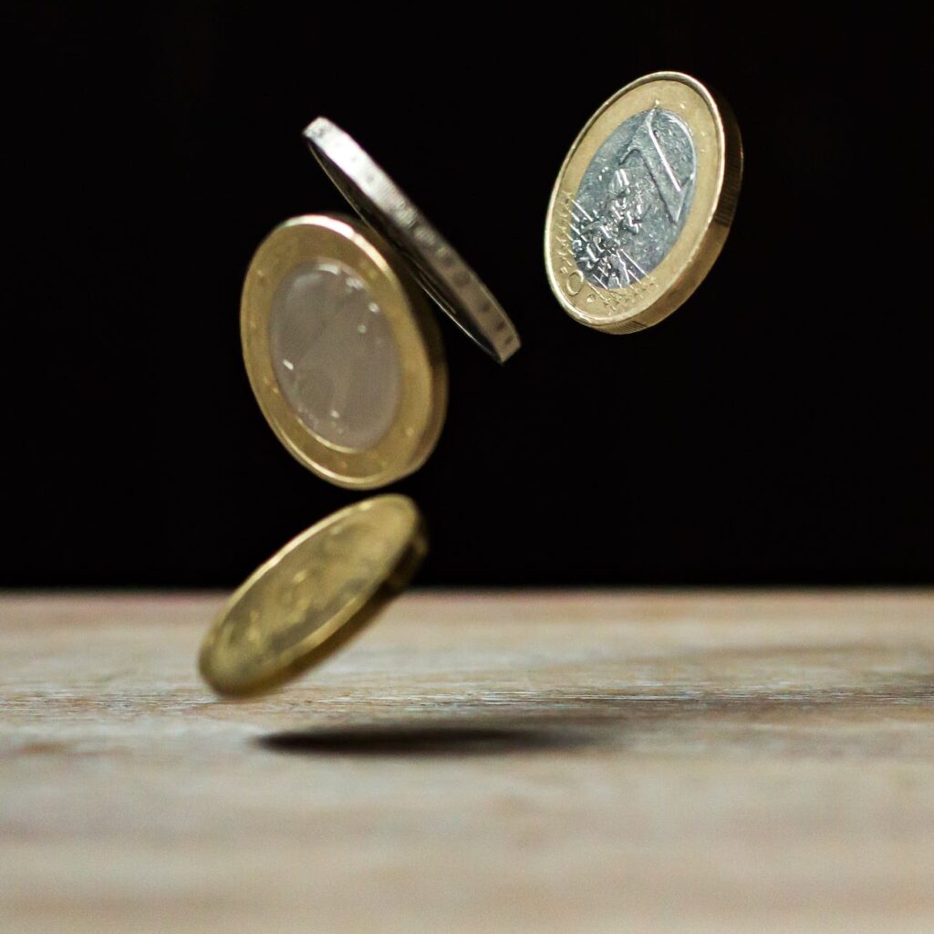 Ein und Zwei Euro-Münzen, die auf einen Holztisch fallen