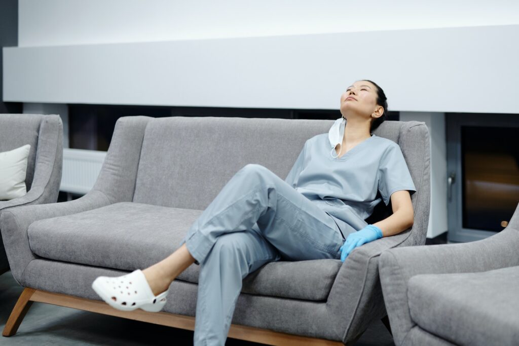 Eine Ärztin sitzt erschöpft auf einer Couch.